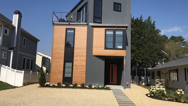 A modern two-story house with a balcony, large windows, and a gravel driveway. - Rehoboth Beach Modern New Build with Elevator (Rehoboth Beach)