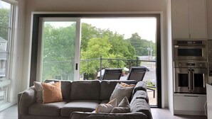 A modern living room with a sectional sofa, a ceiling fan, and a view of a balcony with outdoor furniture. - Rehoboth Beach Modern New Build with Elevator (Rehoboth Beach)