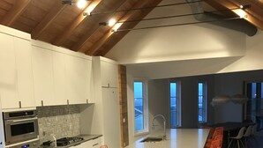 A modern kitchen with white cabinets, stainless steel appliances, and a long island with orange chairs. - Rehoboth Beach Modern New Build with Elevator (Rehoboth Beach)