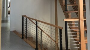 A wooden staircase with a glass railing and metal balusters, leading to an upper floor. - Rehoboth Beach Modern New Build with Elevator (Rehoboth Beach)