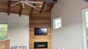 A modern living room with a wooden ceiling, a fireplace, a large flat-screen TV, and a grey sofa. - Rehoboth Beach Modern New Build with Elevator (Rehoboth Beach)