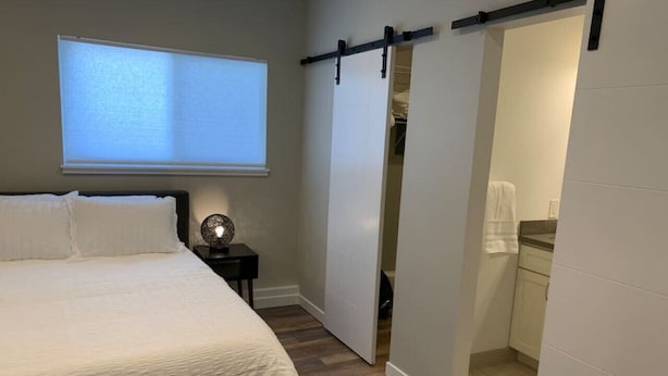 A bedroom with a bed, a nightstand, a wall-mounted projector, and a sliding door leading to a bathroom. - Maple Valley Hummingbird Studio (Maple Valley)