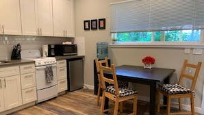A kitchen with white cabinets, a stove, a microwave, and a water dispenser. There is a dining table with two chairs and a vase with flowers. - Maple Valley Hummingbird Studio (Maple Valley)
