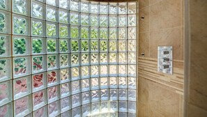 A bathroom with a curved glass partition, a shower area, and a wall-mounted faucet.