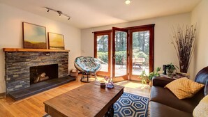 A living room with a stone fireplace, a wooden coffee table, a brown leather sofa, and a large window with a view of greenery.