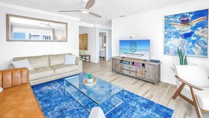 A modern living room with a sofa, coffee table, TV, and artwork. - Gertrude's Siesta | Oceanview, 12-steps Beach, 4-min trolley to Village, tiki-bar, ping-pong! (Siesta Key)