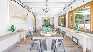 A spacious dining area with a long wooden table, metal chairs, and potted plants. - Gertrude's Siesta | Oceanview, 12-steps Beach, 4-min trolley to Village, tiki-bar, ping-pong! (Siesta Key)