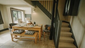 Uma área de refeições com mesa e bancos de madeira, uma escada e vista para o exterior.