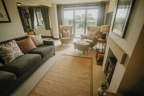 A living room with a grey sofa, patterned cushions, a beige armchair, a small table, and a fireplace.