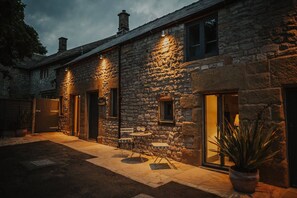 A stone building with a patio area, outdoor seating, and a potted plant. - The Piggery - stylish barn conversion in the heart of the High Peak (Tideswell)