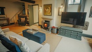 A cozy living room with a fireplace, a television, and a comfortable seating area. - The Piggery - stylish barn conversion in the heart of the High Peak (Tideswell)
