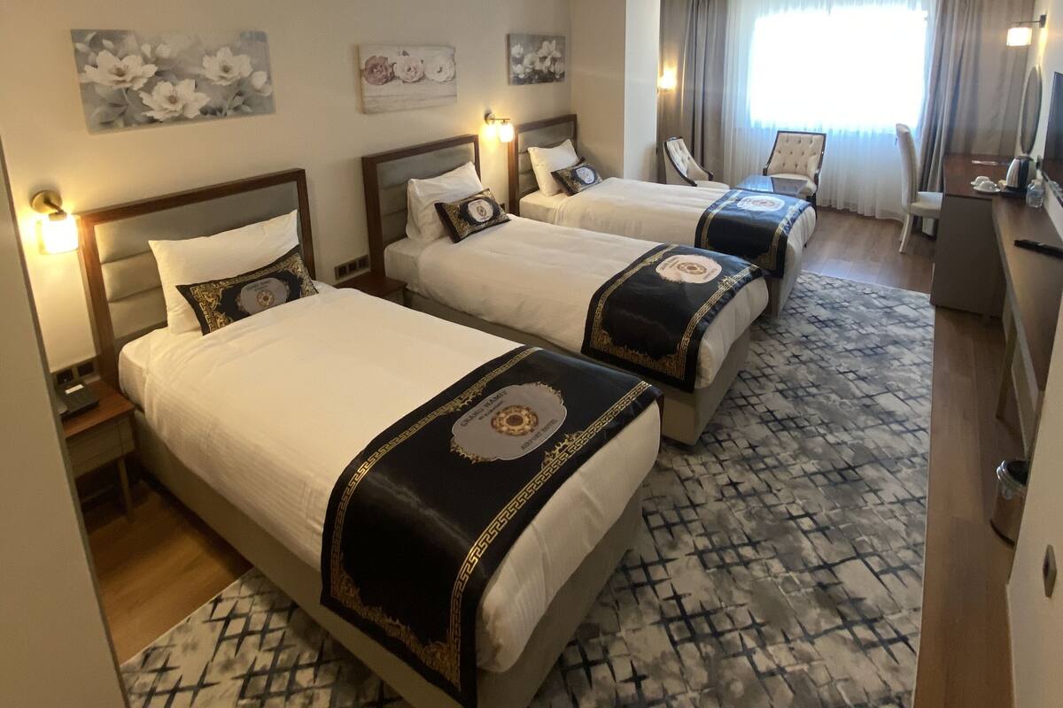A hotel room with three beds, a desk, and a large window with curtains.