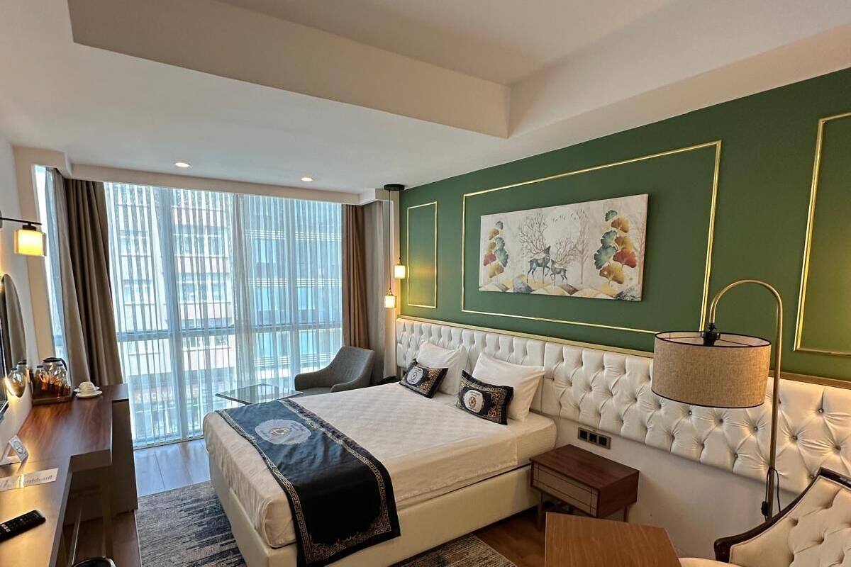 A modern hotel room with a large bed, a sofa, a desk, and a large window.