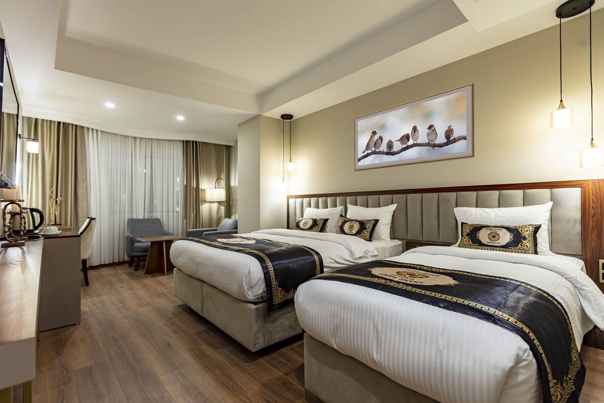 A hotel room with two beds, a desk, a chair, and a large window with curtains.