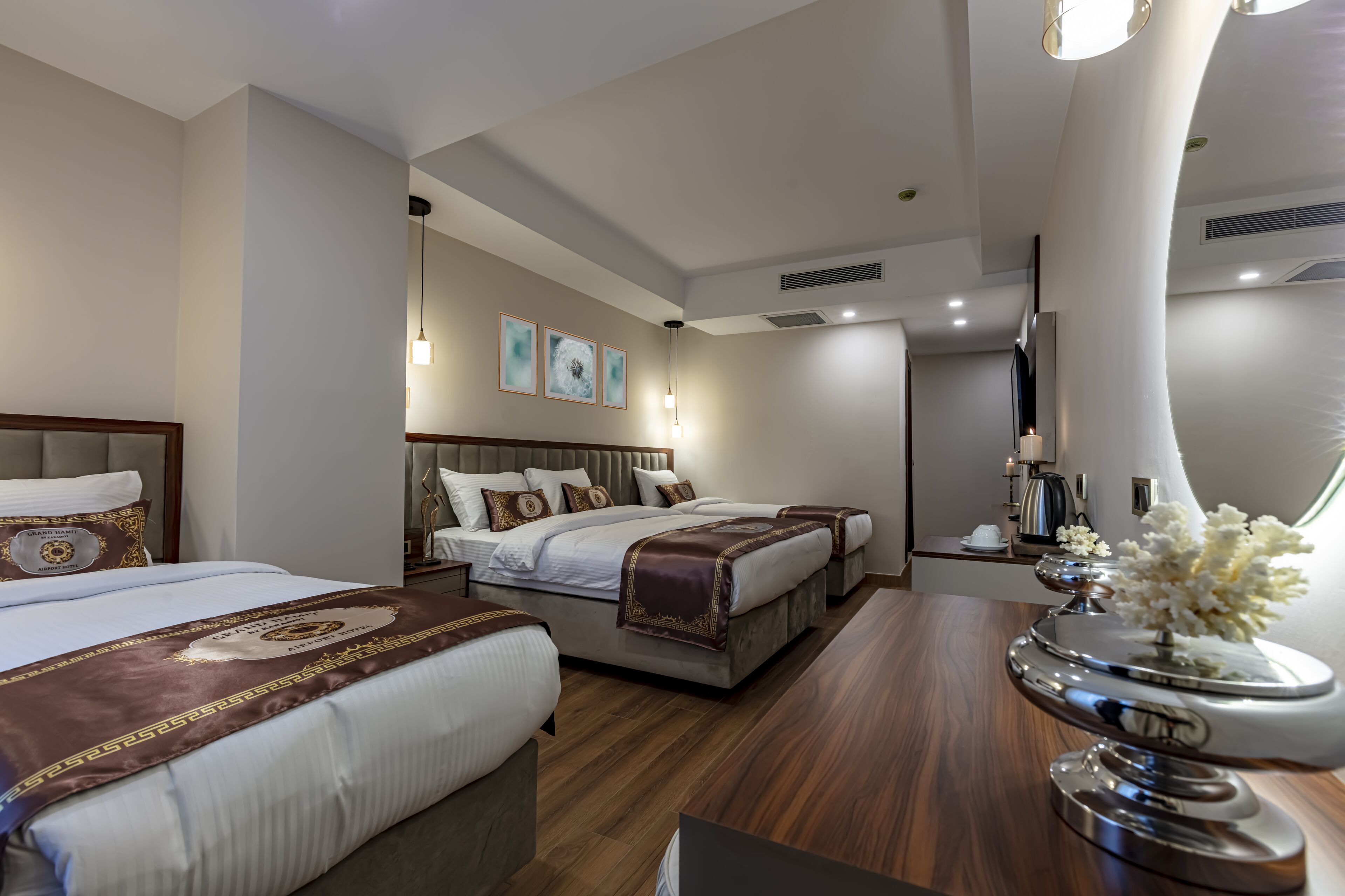 A modern hotel room with two beds, a vanity with a mirror, and a decorative vase.
