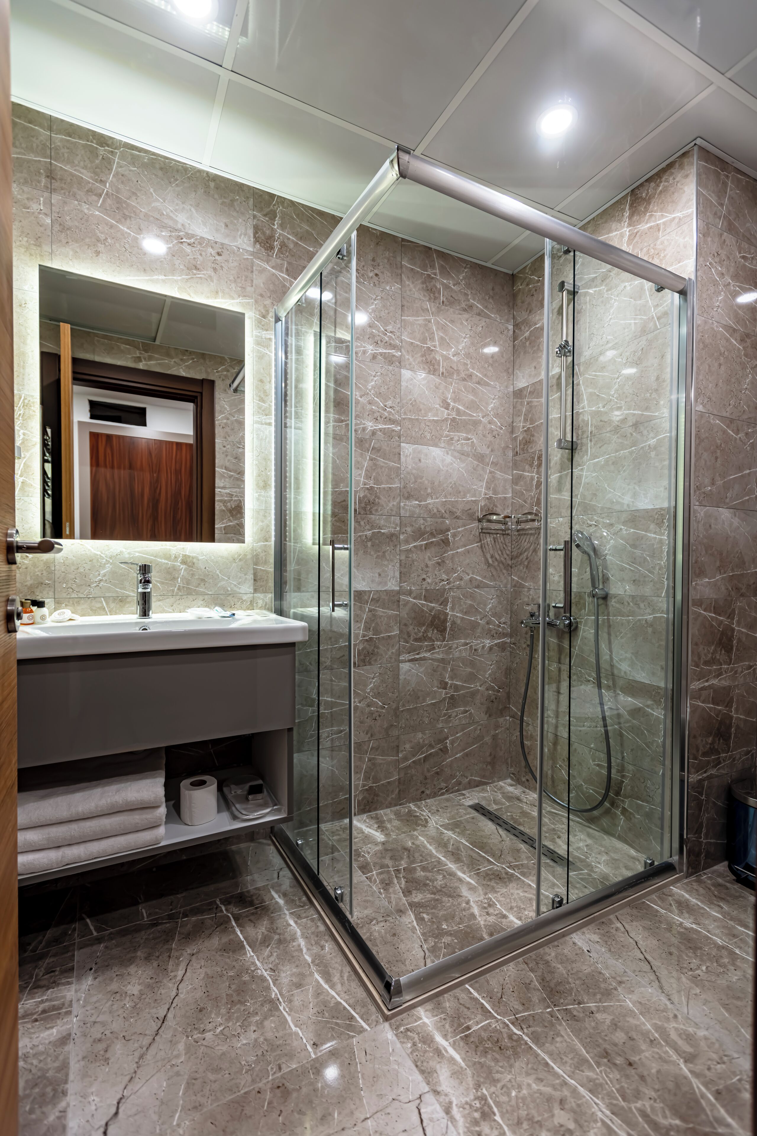 A modern bathroom with a glass-enclosed shower, marble flooring, and a vanity with a mirror and sink.