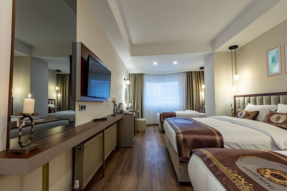 A hotel room with a large bed, a smaller bed, a desk with a flat-screen TV, a mirror, and a window with curtains.