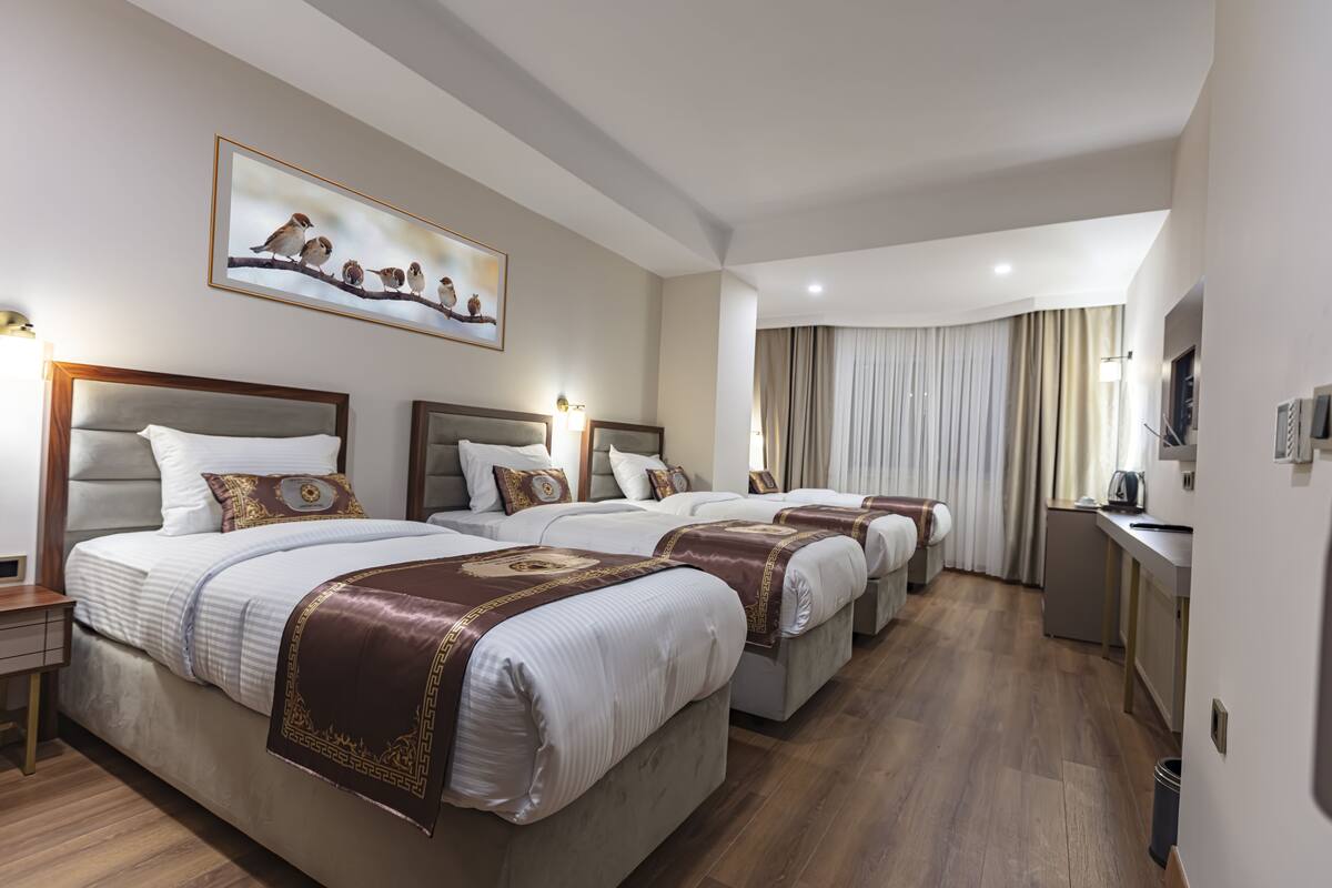 A hotel room with four beds, a painting of birds on the wall, and a view of the city.