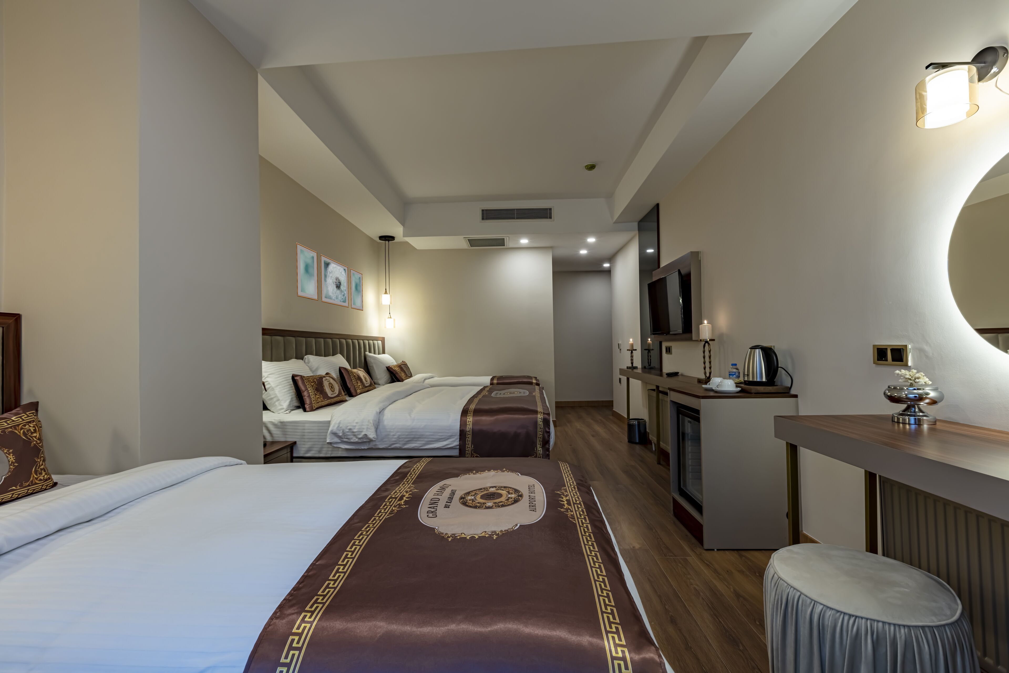 A hotel room with two beds, a desk, a mirror, and a small stool.