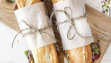 Two sandwiches on a wooden board tied with twine.