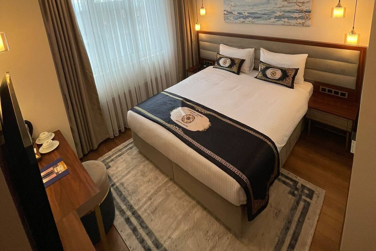 A hotel room with a large bed, a desk, a chair, a painting on the wall, and a window with curtains.