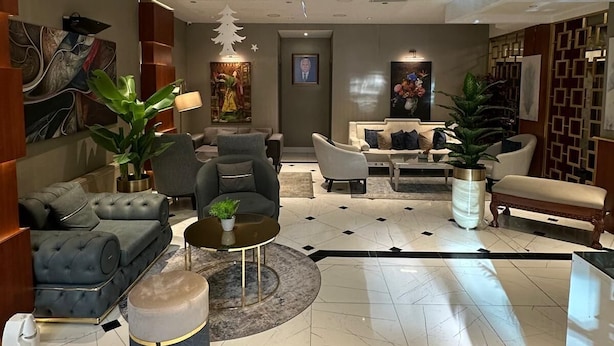 Een moderne hotel lobby met een centraal zitgedeelte, een groot schilderij links en een decoratieve boom aan het plafond.