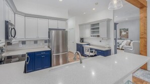 Une cuisine moderne avec des meubles blancs et bleus, des appareils en acier inoxydable et un grand îlot central doté d’un évier.