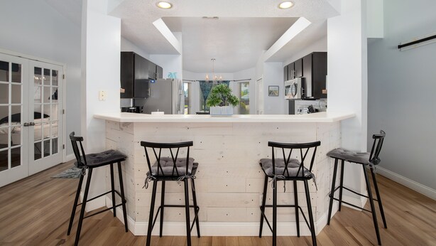 Una cocina moderna con una isla blanca, taburetes de bar y una planta en maceta.