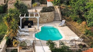 Una villa in pietra con piscina, immersa nel verde e circondata da un pendio roccioso.