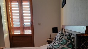 Una camera da letto con un letto, un comodino con una lampada, una finestra con persiane e un piccolo tavolo con una candela.