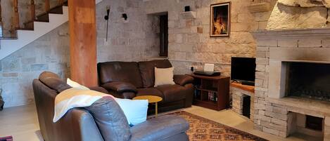 A living room with a stone fireplace, leather sofa, and a television.