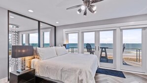 Ein Schlafzimmer mit Bett, Deckenventilator, Nachttisch und Blick auf den Strand durch große Schiebetüren.