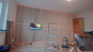 Une pièce avec un mur à lattes, une échelle, un aspirateur et un téléviseur fixé au mur.