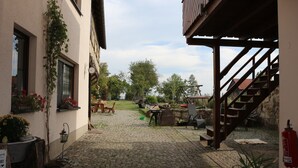 A courtyard with cobblestone flooring, a wooden staircase, and outdoor seating. - Ferienwohnung Brunow ,,kerstin" In der Natur Zuhause (Neundorf(bei Schleiz))