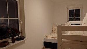 A narrow room with a bunk bed, a window with a view of the outside, and a small shelf with decorative items. - Ferienwohnung Brunow ,,kerstin" In der Natur Zuhause (Neundorf(bei Schleiz))
