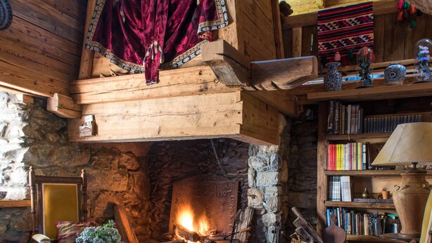 A cozy log cabin interior with a stone fireplace, wooden bookshelves, and plush furnishings. - Arthaus Megeve (Demi-Quartier)