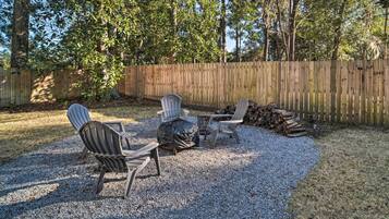 A backyard with a wooden fence, two Adirondack chairs, a small table, and a fire pit with logs.