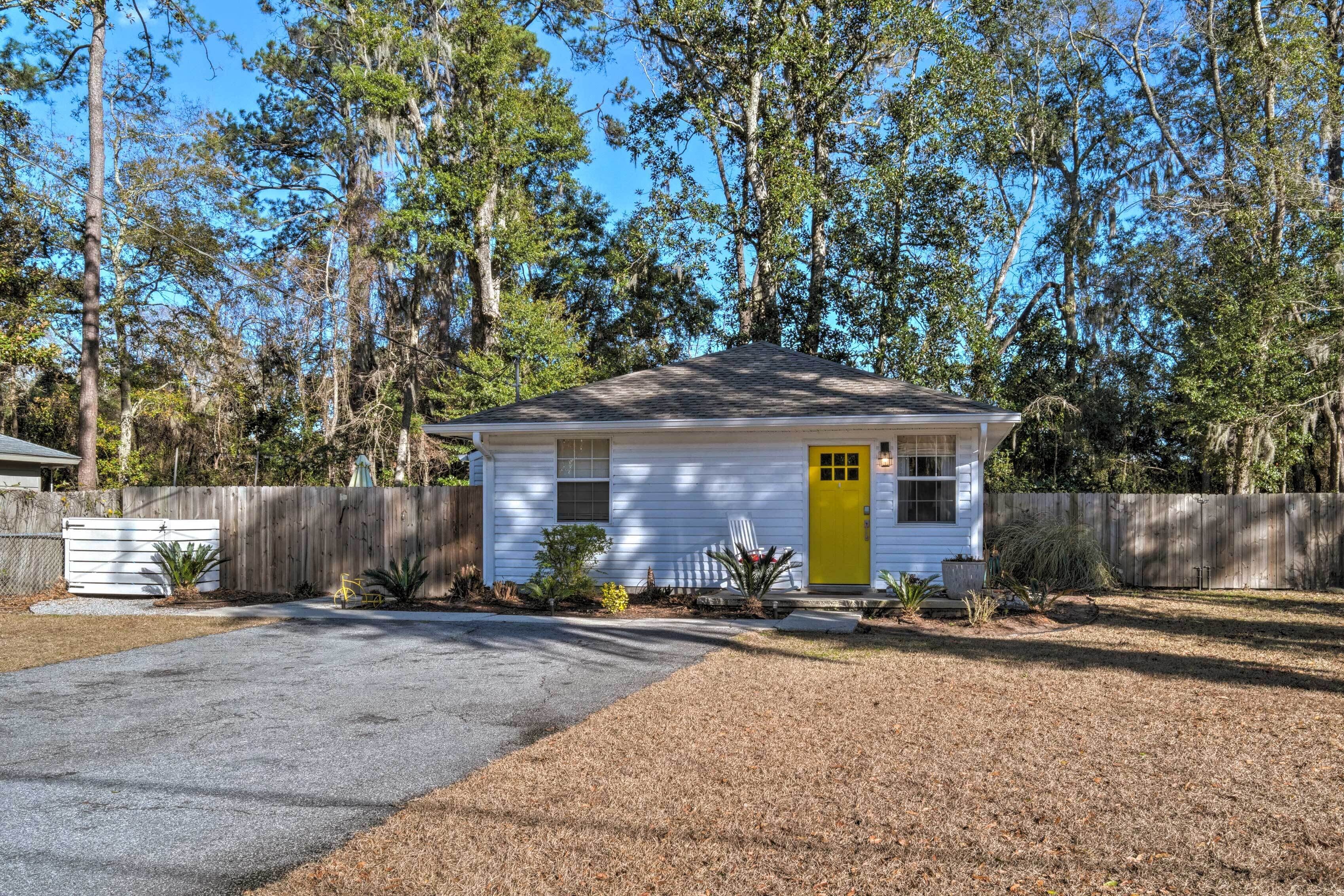 A small white house with a yellow door, surrounded by a wooden fence and trees.