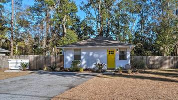 A small white house with a yellow door, surrounded by a wooden fence and trees.