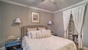 Ein Schlafzimmer mit einem Bett, zwei Nachttischen mit Lampen, einem Deckenventilator, einem gerahmten Bild an der Wand und einem Kleiderschrank mit einer Leiter.