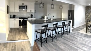 A modern kitchen with white cabinets, a central island with bar stools, stainless steel appliances, and pendant lighting. - Modern Ranch House~Great for Big Groups! Salt Water Pool + Spa  (Desert Hot Springs)