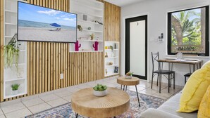 Un salon moderne avec un téléviseur, des étagères en bois, une table basse ronde et un coin repas comprenant des chaises et une table.