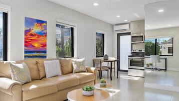 A modern living room with a beige sofa, a round coffee table, and a dining area with a small table and chairs.