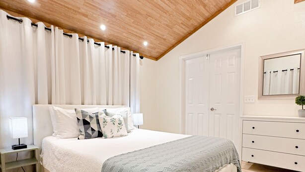 Un dormitorio con cama, mesitas de noche, cómoda, espejo e iluminación empotrada en el techo.