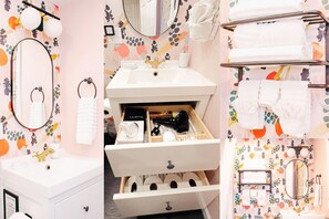 A bathroom with a white vanity, a mirror, a towel rack, and a storage drawer.