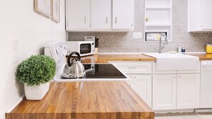 Una cocina moderna con armarios blancos, microondas, hervidor y un lavamanos.