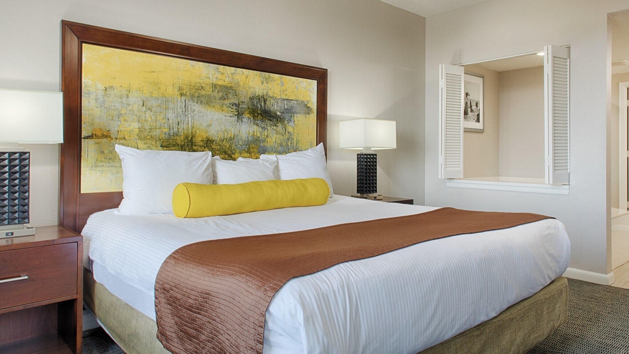 A hotel room with a large bed, a bedside table, a lamp, and a painting on the wall.