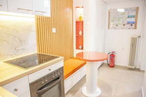 A modern kitchen with a built-in oven, a wooden panel wall, a small table, and a fire extinguisher.