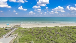 Ein Strand mit einer Holzpromenade, die zum Ufer führt, bewölkter Himmel und Meer.
