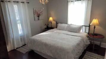 Un dormitorio con una cama grande, dos mesitas de noche con lámparas, una araña y una ventana con cortinas.
